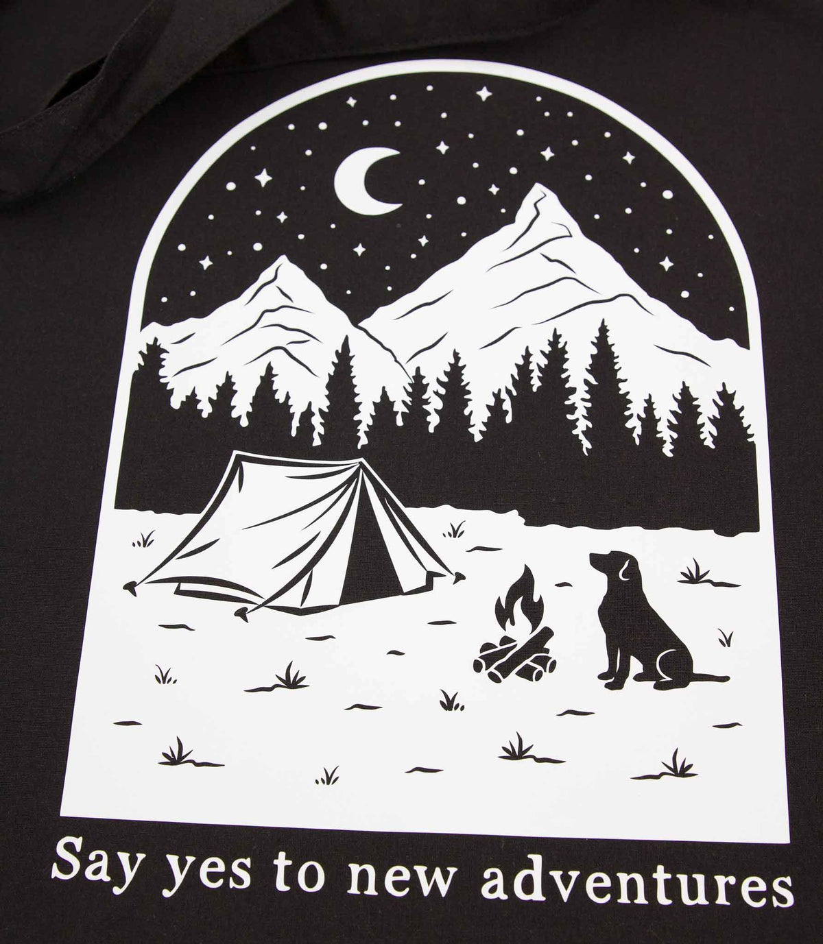 Musta kangaskassi, jossa on käsinpiirretty ja painettu kuva koirasta ja maisemasta, jonka alla on teksti Say yes to new adventures.