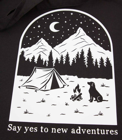 Musta kangaskassi, jossa on käsinpiirretty ja painettu kuva koirasta ja maisemasta, jonka alla on teksti Say yes to new adventures.