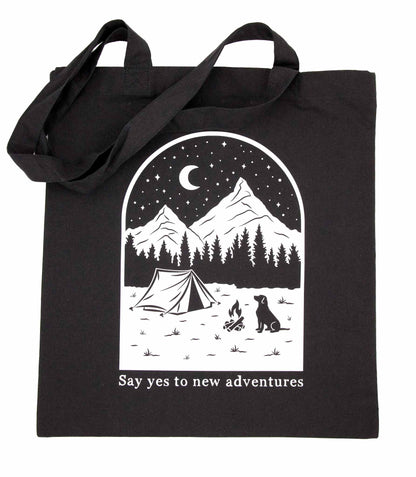 Musta kangaskassi, jossa on käsinpiirretty ja painettu kuva koirasta ja maisemasta, jonka alla on teksti Say yes to new adventures.